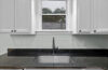 Kitchen sink beneath a window with white cabinets and a dark worktop