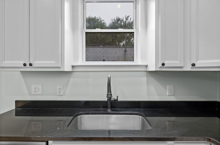 Three things to consider before renovating your kitchen 6 Kitchen sink beneath a window with white cabinets and a dark worktop